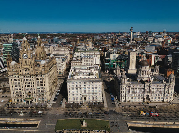 Aerial view of Liverpool featuring the Three Graces, buildings, roads, and skyline under a bright blue sky