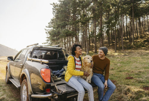 Couple sitting on a pickup truck with a dog